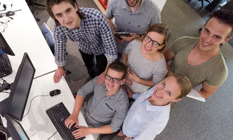 Young professionals smiling around computer in modern office.