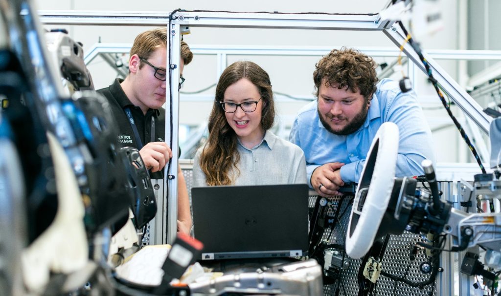 Team collaborating on laptop in industrial factory workspace.