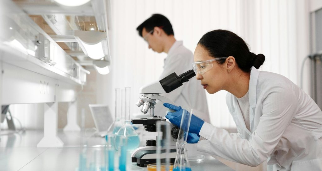 Researchers in lab coats studying microscope in laboratory.