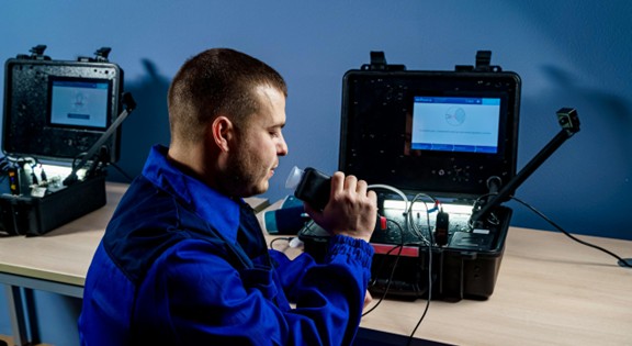 Technician using handheld diagnostic device in lab setting.