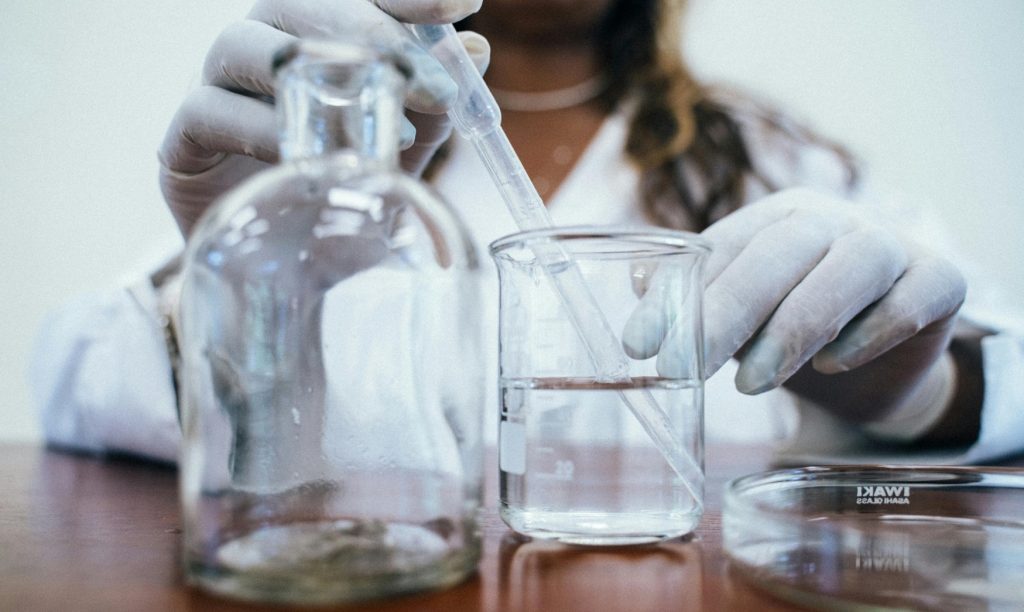 Scientist with gloves transferring liquid into beaker in lab.